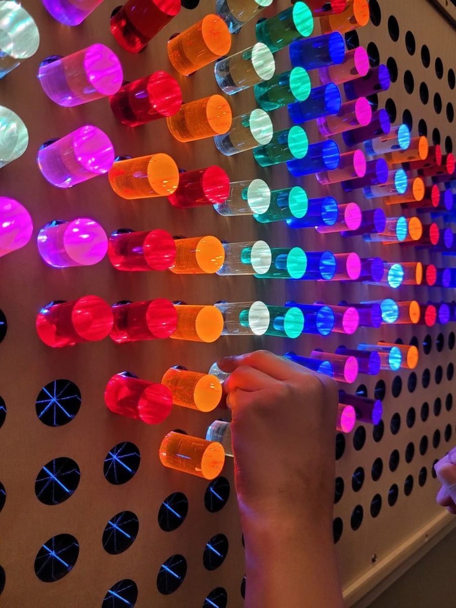 A child placing glowing coloured pegs on a light board.
