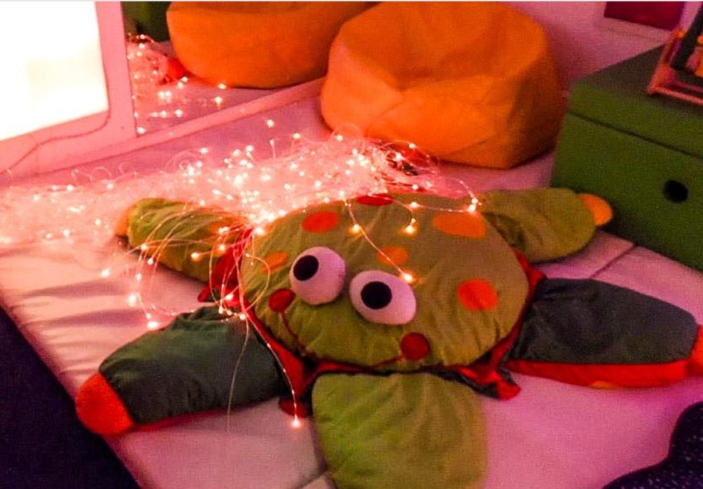 A light-up turtle cushion glowing among soft bean bags in the sensory room.